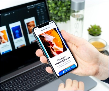 Hand holding the phone with the
              laptop in the background
